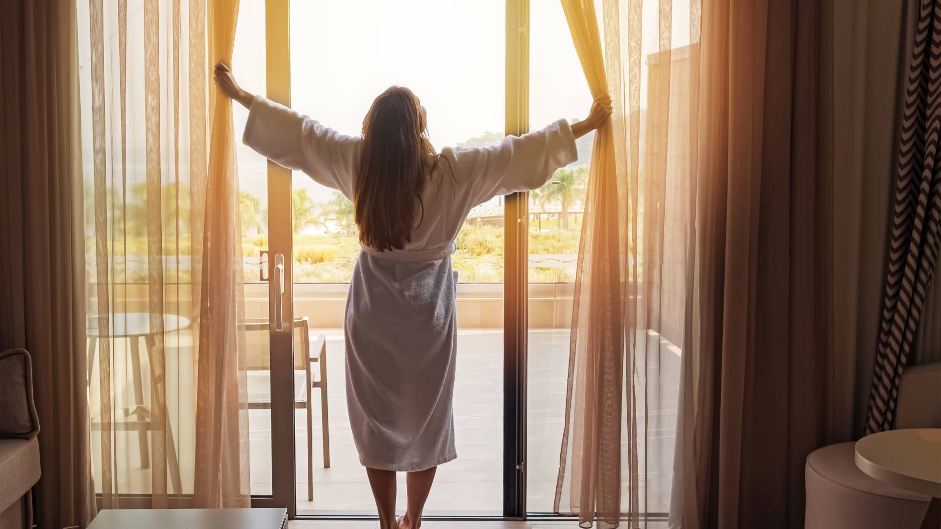 Woman opens the curtains in the hotel room in the morning